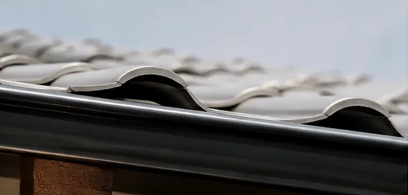 Calha galvanizada instalada sob telhado de telhas cerâmicas, com fixação alinhada ao beiral.